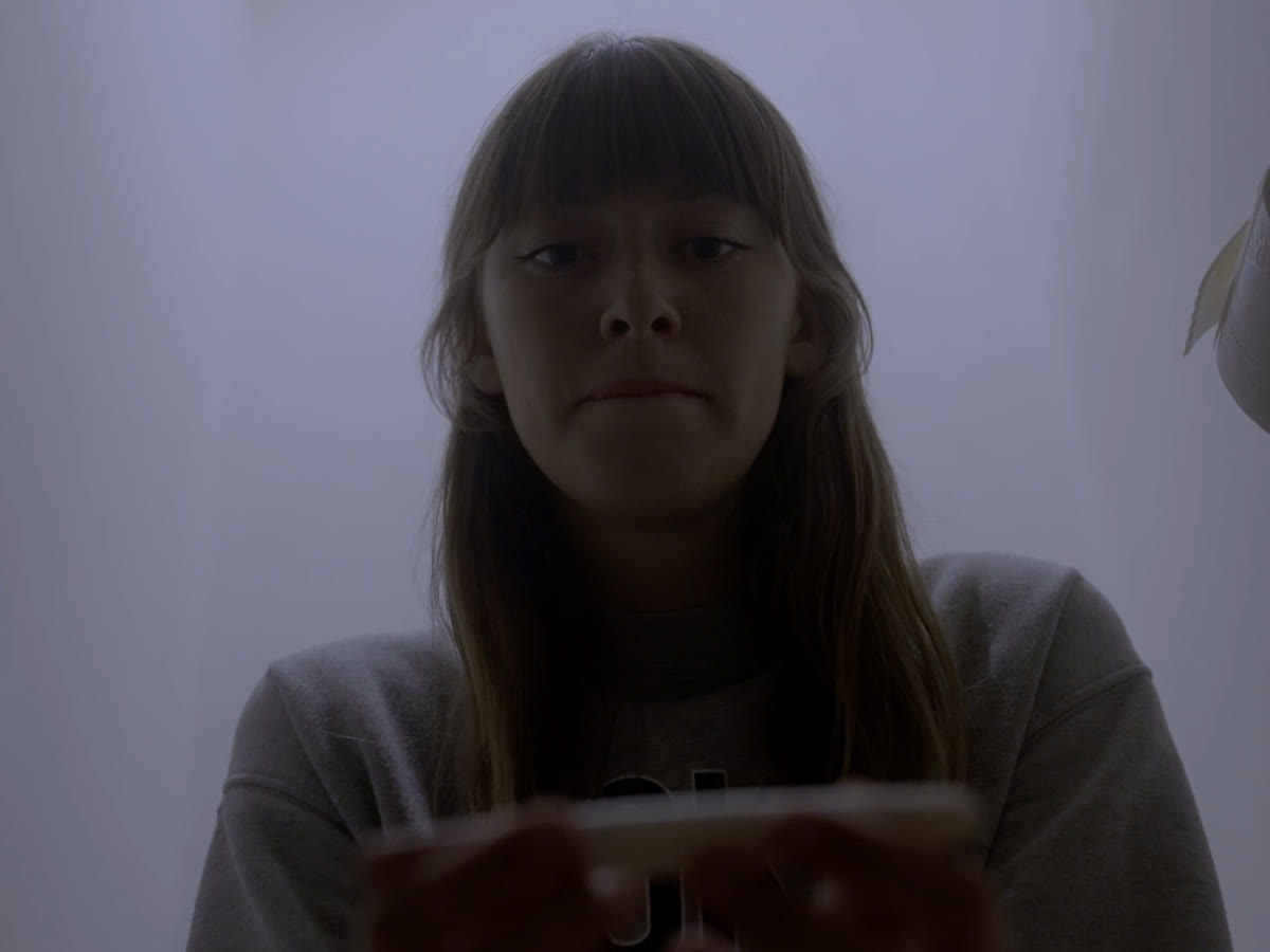 Still from the short film Amber: a girl looking down at her phone, backlit