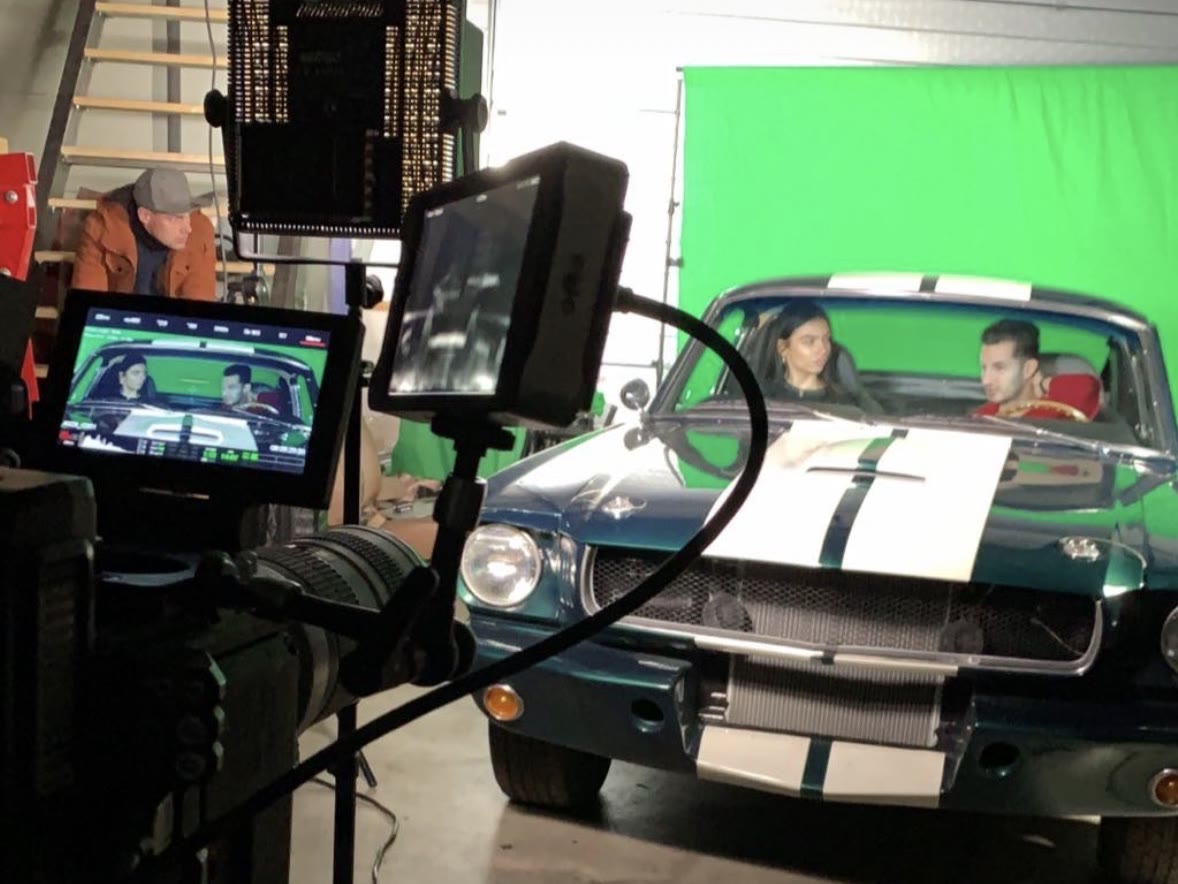 On set: camera and monitor in front of a classic Mustang with two actors against a green screen